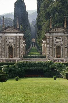 an ornate garden with hedges and trees in the background