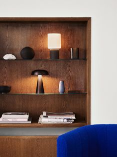 a blue chair sitting in front of a wooden shelf filled with vases and lamps