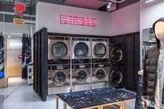 a room filled with lots of clothes and washing machines in front of a neon sign