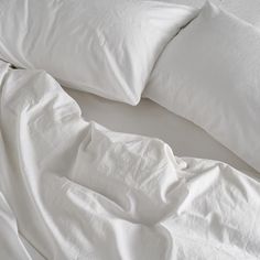 an unmade bed with white sheets and pillows