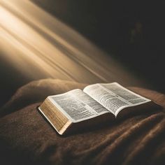 an open book sitting on top of a bed next to a light shining through the window