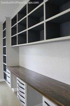 an empty room with white cabinets and black shelvings on the wall, and a wooden counter in front of it