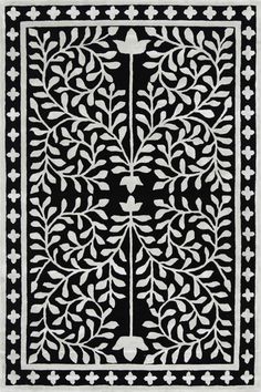 an intricately designed black and white rug with leaves on the border, in front of a