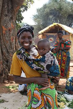 a woman holding a baby in her arms while sitting on the ground next to other people