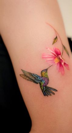 a hummingbird flying towards a flower on the back of a woman's shoulder