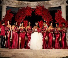 a bride and her bridal party posing for a photo in front of red flowers