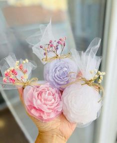 hand holding three soap balls with flowers on them and ribbons tied to the top, in front of a window