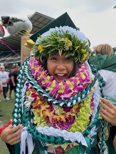 a woman wearing leis and flowers on her head at a football game with other people in the background