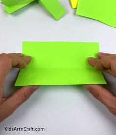 two hands holding a piece of green paper over a white table with sticky notes on it