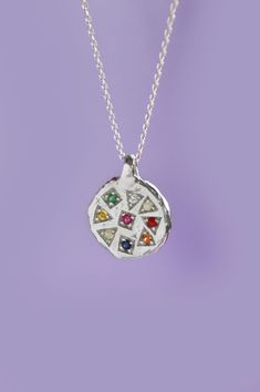 a small silver pendant with multicolored stones on the front and back of it