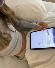 a woman laying in bed with her legs crossed and writing on an electronic device next to her stomach