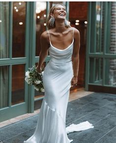 a woman in a white dress is walking down the street smiling and holding a bouquet