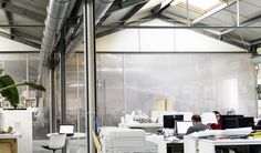 an office filled with lots of computers and people working on their desks in front of large windows