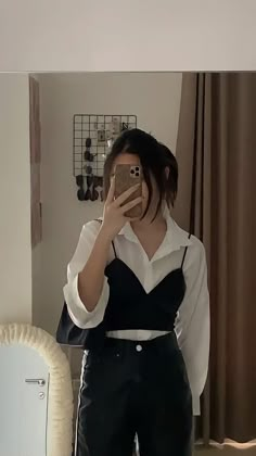 a woman taking a selfie in front of a mirror wearing black pants and a white shirt