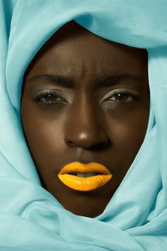 a woman's face with yellow lipstick and blue shawl over her head, looking into the distance