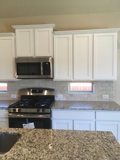 a kitchen with white cabinets and granite counter tops, stainless steel appliances and black stove top oven