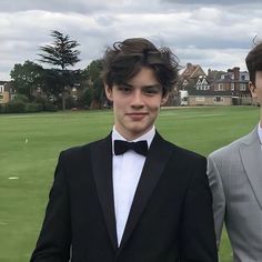 two young men in tuxedos standing next to each other on a golf course