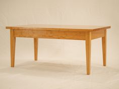 a wooden table sitting on top of a white floor next to a plain white wall