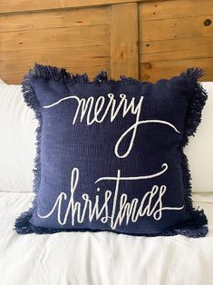 a blue pillow that says merry christmas on it sitting on top of a white bed