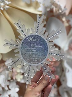 a person holding up a snowflake shaped ornament in front of flowers