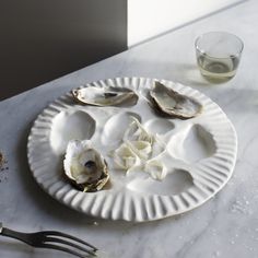 oysters on a paper plate next to a fork and glass with water in it