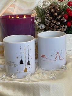 two coffee mugs sitting next to each other on a table with candles in the background