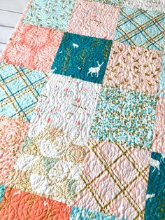 a colorful quilt is laying on top of a white tablecloth with blue, pink and orange squares