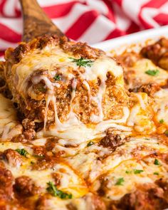 a wooden spoon scooping out some lasagna sauce from a casserole dish