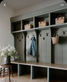 a wooden bench with baskets and coat hooks on it's sides, next to a vase with flowers