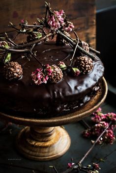 a chocolate cake topped with berries and flowers on top of a wooden table next to some branches