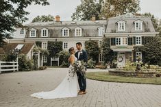 a bride and groom standing in front of a large house on a cobblestone driveway