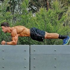 a shirtless man is doing push ups on a metal wall with trees in the background