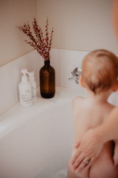 a naked woman sitting in a bathtub next to a brown bottle with flowers on it