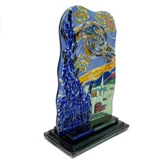 a blue glass sculpture with an artistic painting on it's face and trees in the background