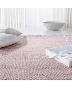 a pink rug with white pillows and a glass of water on the floor next to it