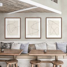 three framed art pieces hang on the wall above a couch and two tables with stools