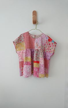 a pink and yellow patchwork top hanging on a wall next to a wooden hanger