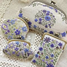 three purses with blue flowers on them sitting on a lace doily tablecloth