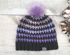 a knitted hat with a purple pom - pom sitting on top of it