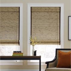 a living room filled with furniture and two windows covered in bamboo blind shades on top of them