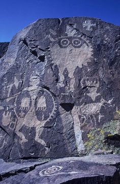 rock art depicting people and animals on the side of a mountain with blue sky in background