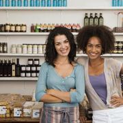 two women standing next to each other in front of shelves filled with bottles and jars