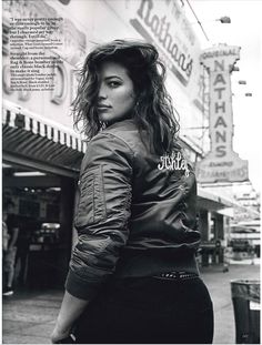 black and white photograph of a woman standing in front of a store with her back to the camera