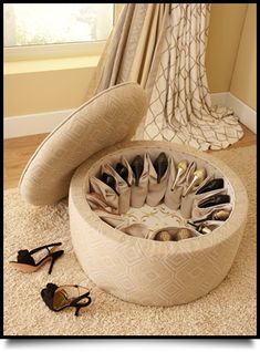 a round foot stool with many pairs of shoes in it on the floor next to a window