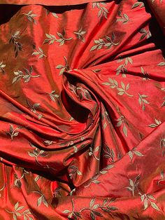 the fabric is red and gold with white flowers on it, as well as green leaves