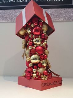 a red and gold christmas ornament on display in a box with the name graeulie