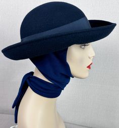 Body is a navy blue felt with the rounded crown and wide curled brim. Attached underneath is a thick blue knit scarf that can be tied in the front or wrapped around the neck and tied in the back. A great hat for winter. Excellent condition with no issues. No size or maker is indicated. Inner circumference is 22 inches. Crown rises 3 1/2 inches and the brim extends 3 inches. Retro Wide Brim Cloche Hat For Winter, Blue Wide Brim Hat For Winter, Blue Fedora Felt Hat For Winter, Fitted Blue Cloche Hat For Winter, Navy Curved Brim Hat For Winter, Retro Adjustable Felt Hat For Winter, Blue Formal Winter Hat, Fitted Blue Felt Hat For Winter, Vintage Solid Felt Hat For Winter