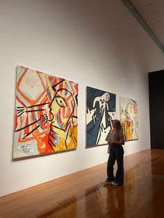 two people looking at paintings on display in an art gallery with wood floors and white walls