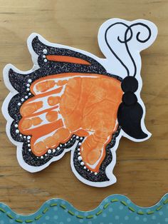 an orange and black butterfly shaped paper cutout sitting on top of a wooden table