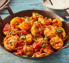 a skillet filled with potatoes and tomatoes on top of a wooden table next to a cup of milk